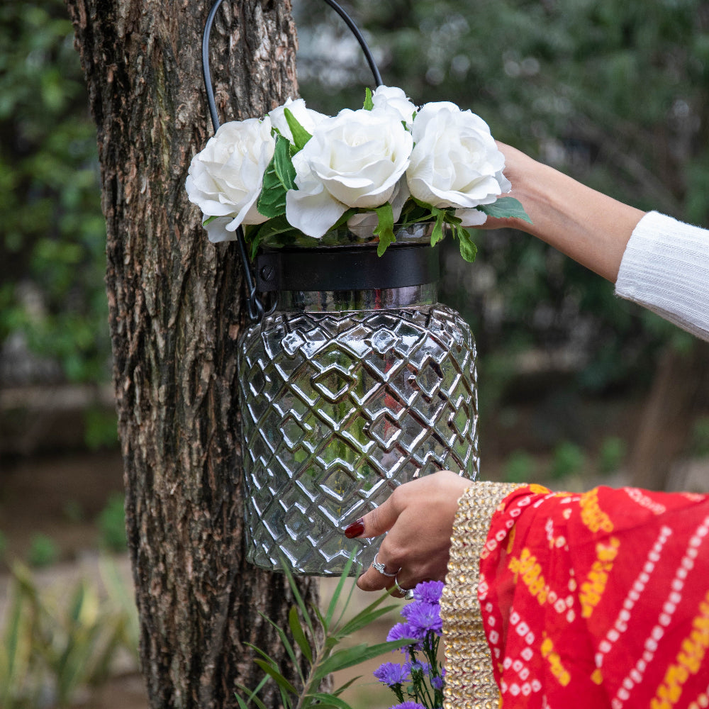 Person holding a silver lantern with white flowers against a tree