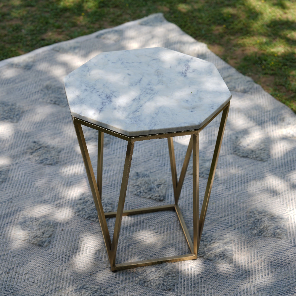 Hexagonal marble table with gold metal base on a textured outdoor rug