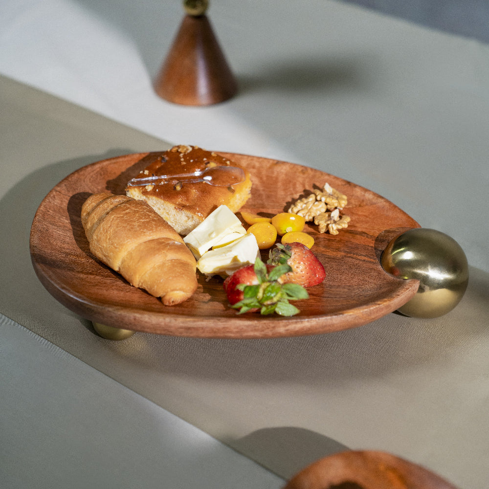 Wooden plate with pastries, fruits, and a small cake on a light surface.