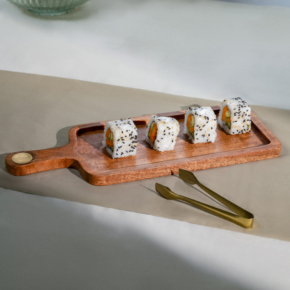 Wooden tray with sushi rolls and gold tongs on a neutral background