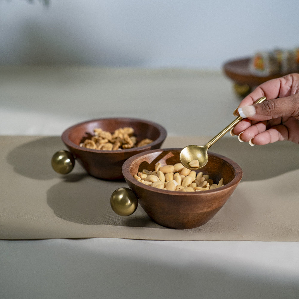 Person using a gold spoon to serve food from a wooden bowl on a beige surface.