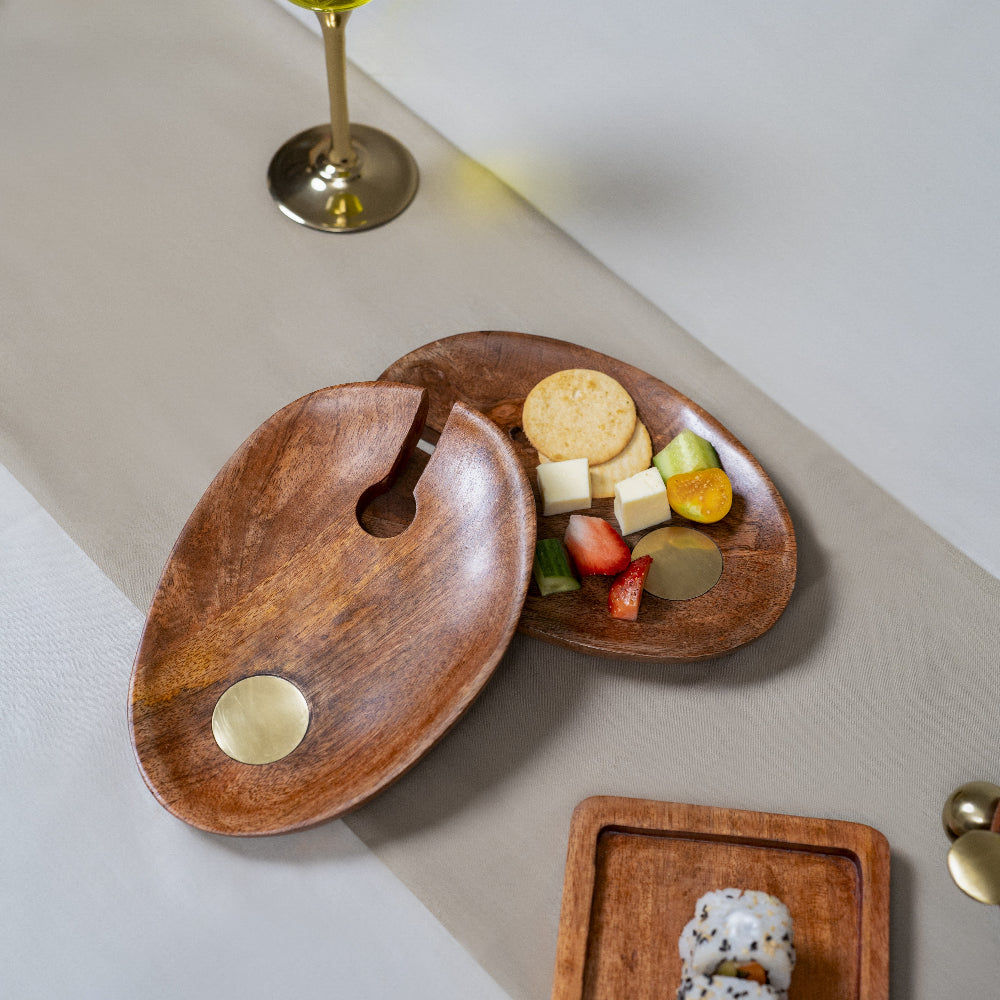 Wooden appetizer platter with cheese, fruits, and crackers on a light surface.