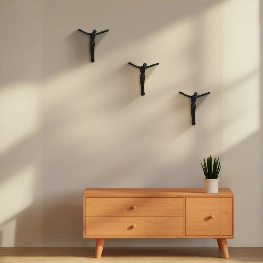 Wooden dresser with a potted plant against a beige wall with three black wall hooks.
