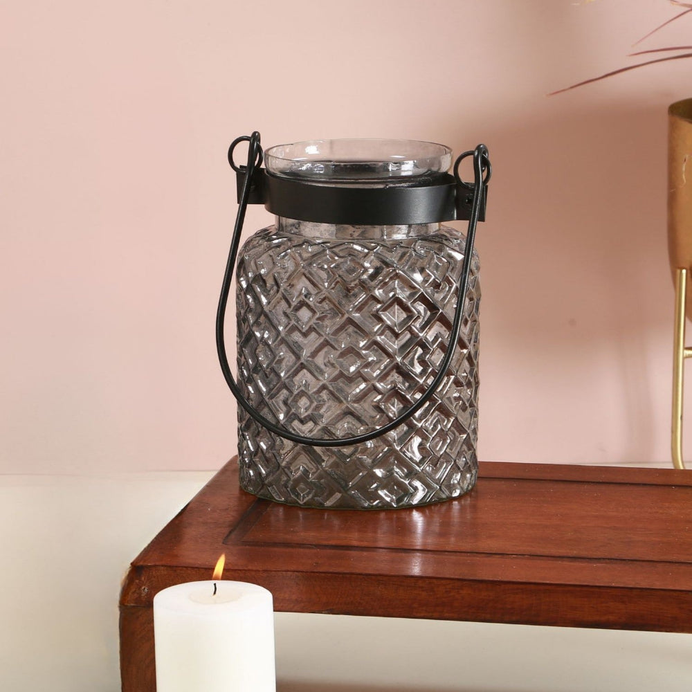 Decorative glass lantern with a black handle on a wooden surface with a pink background
