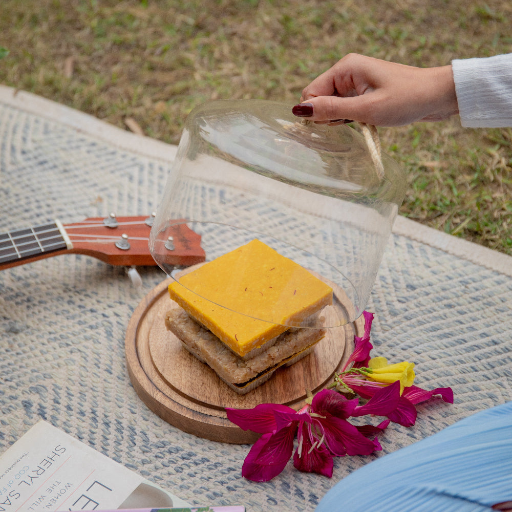 Glass cloche over a cheese sandwich on a wooden board with flowers and a guitar in the background