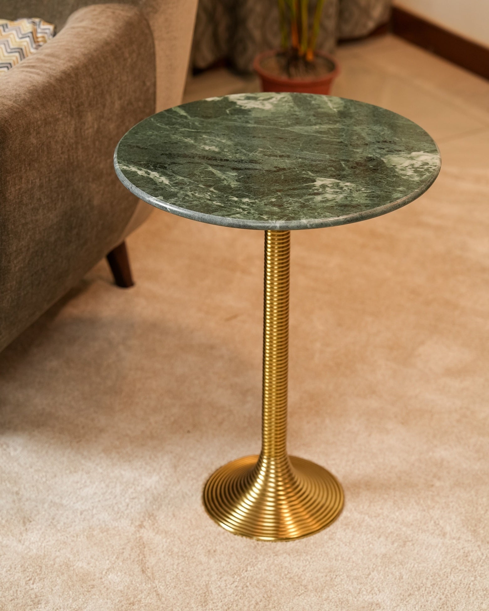 Small round table with green marble top and gold base in a room setting.