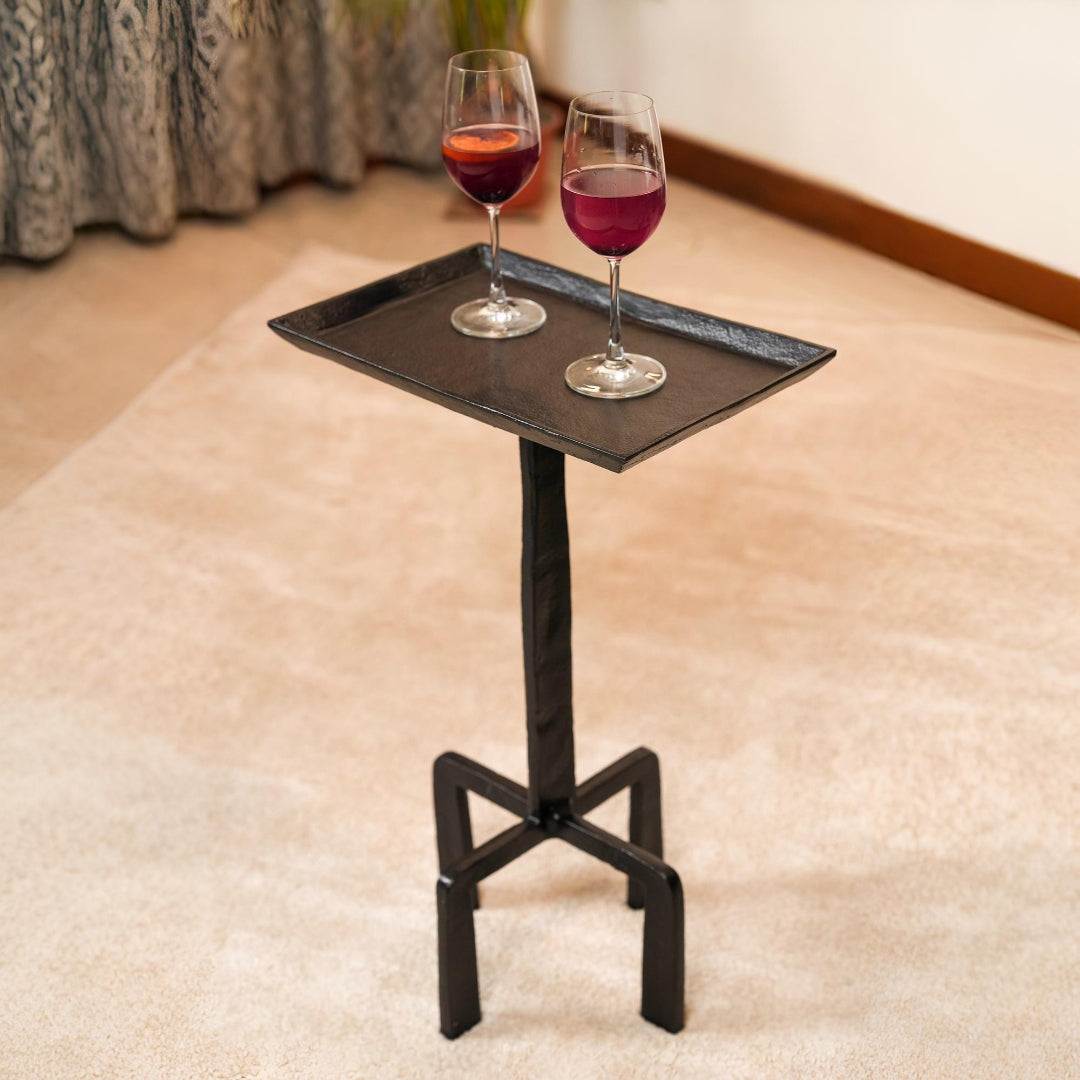 Black metal tray table with two wine glasses on a carpeted floor.