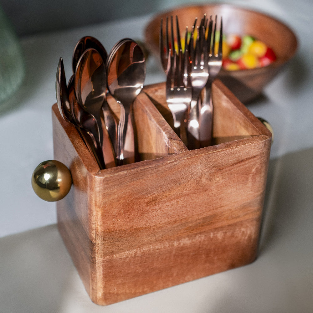 Rose gold cutlery set in a wooden holder on a neutral background