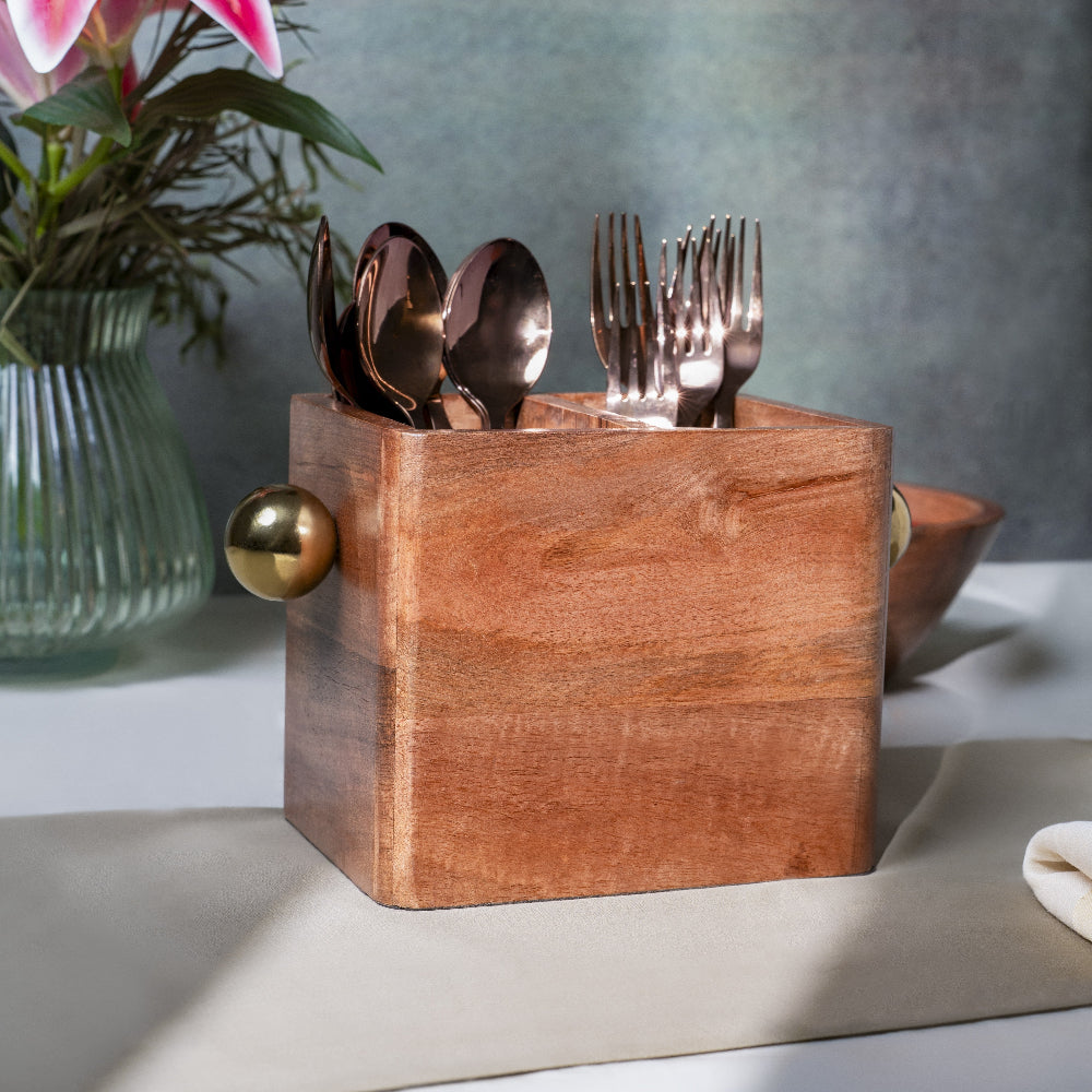 Wooden utensil holder with cutlery on a table with a vase of flowers in the background