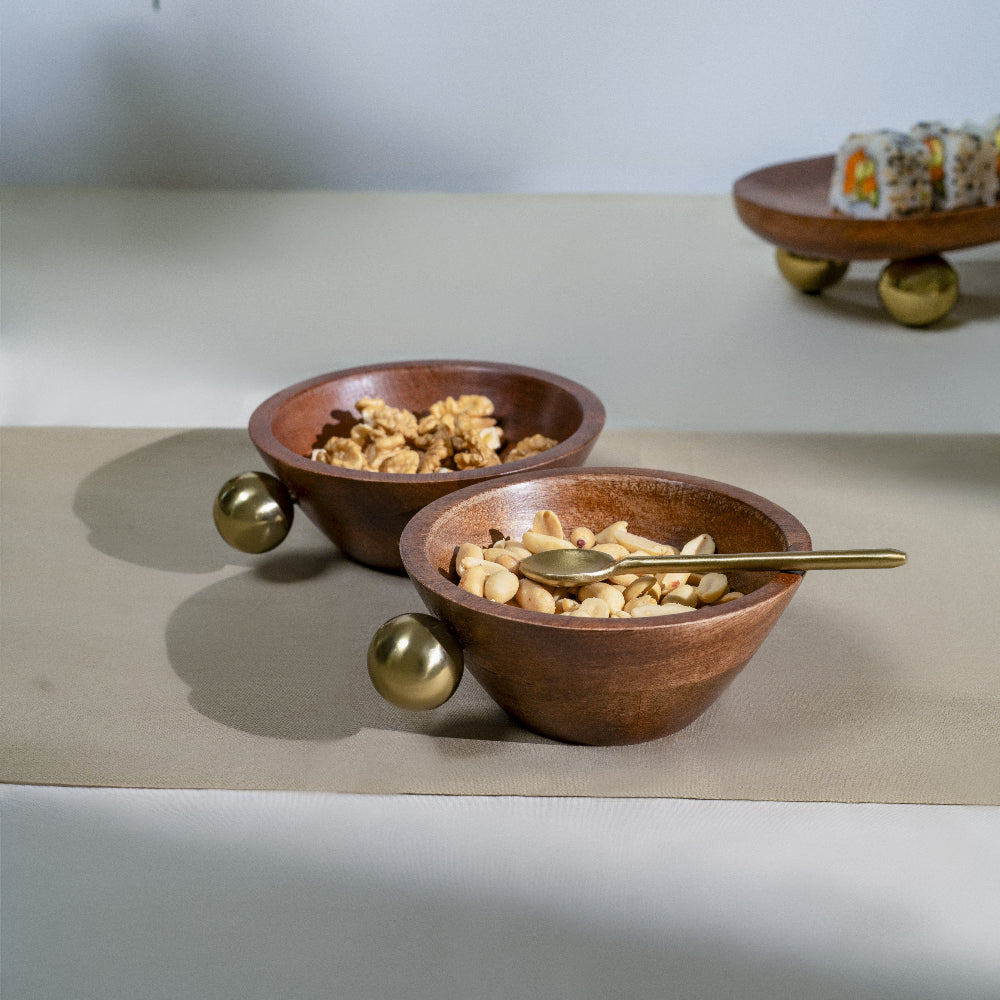 Two wooden bowls with snacks on a light surface, one with a gold spoon.
